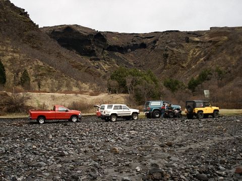 1996 Ford Bronco - Multiple off-road vehicles are parked on a rocky surface near a mountainous area.