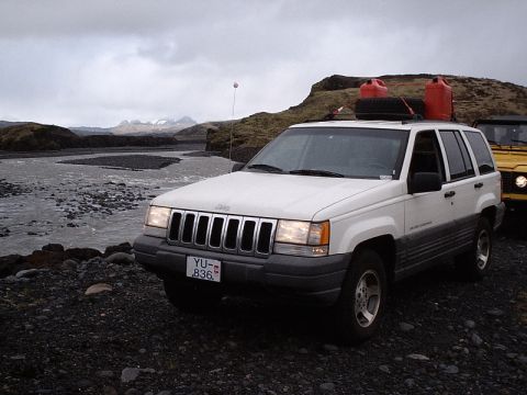 1996 Ford Bronco - A white Jeep Grand Cherokee is parked near a river with a yellow vehicle behind it.