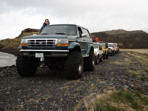 1996 Ford Bronco - A line of off-road vehicles, including a 1996 Ford Bronco, travel on a rocky path under an overcast sky.