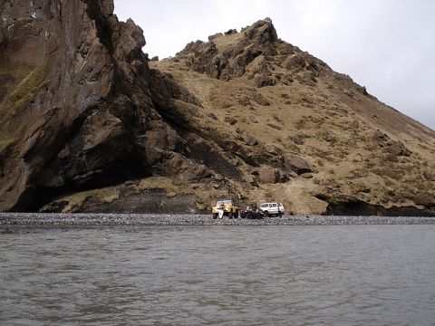 1996 Ford Bronco - Two off-road vehicles are parked on a rocky shore with a large mountain in the background.