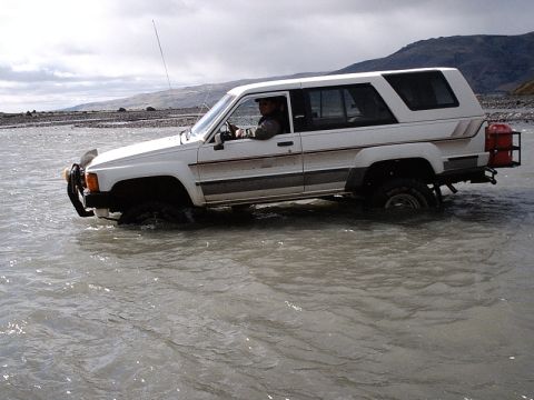 1996 Ford Bronco - White 1984 Toyota 4Runner navigates shallow river water, with a spare gas can attached to the rear.