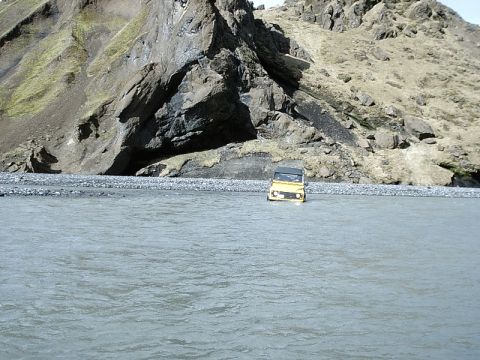 1996 Ford Bronco - A yellow SUV navigates a riverbed, with a dramatic mountain landscape behind it.