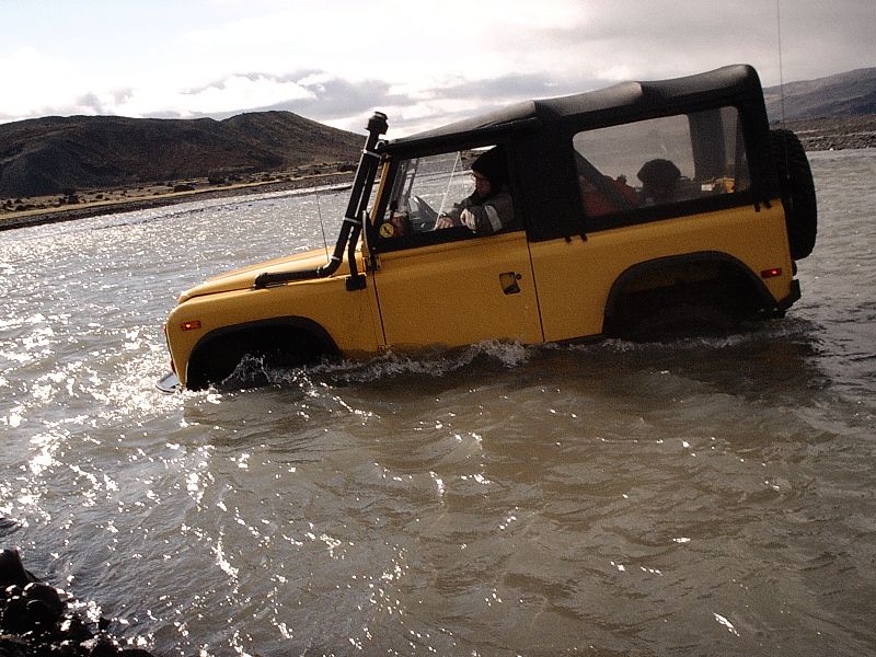 Yellow soft-top 4x4 with snorkel fording a muddy river
