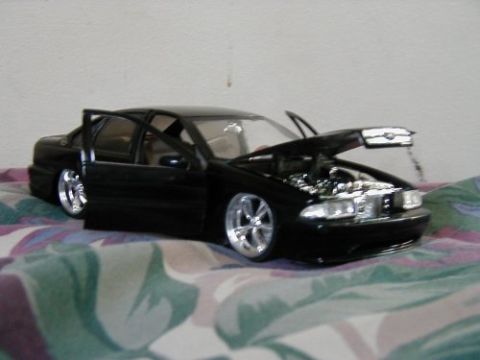 1997 Ford Taurus - A black toy car with its doors and hood open sits on a patterned surface.