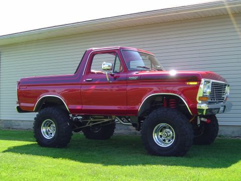 1978 Ford Bronco - Red full-size Ford Bronco with a tall suspension lift, chrome rims and oversized mud tires parked beside a house on a lawn.