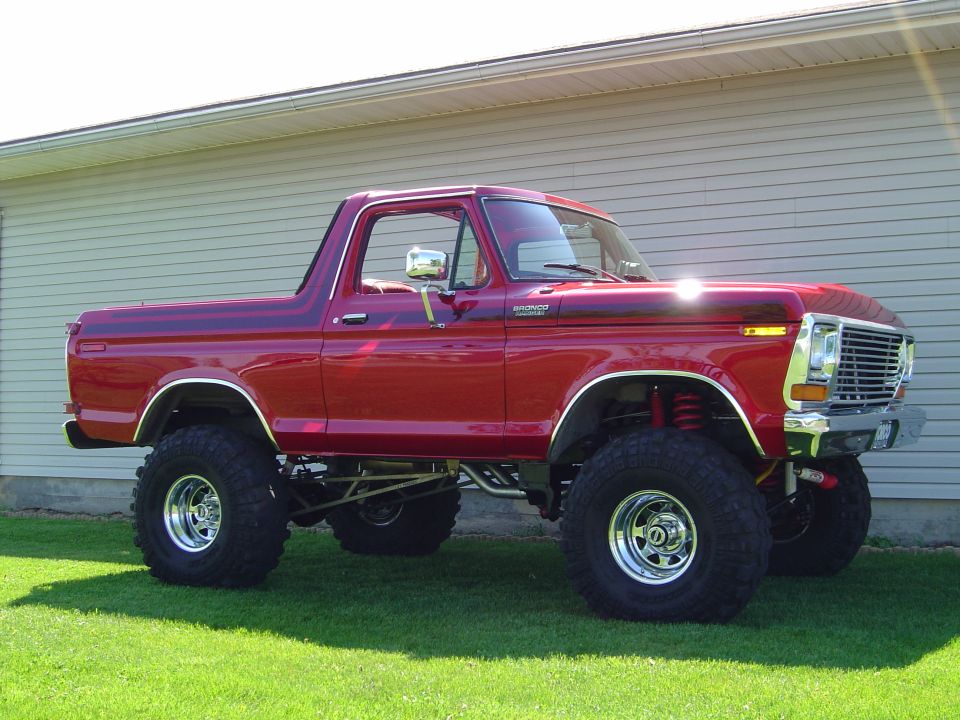Red lifted 1978-79 Ford Bronco on chrome wheels and mud tires parked on grass