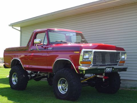 1978 Ford Bronco - A candy-red 1978 Ford Bronco with a lifted suspension, chrome front bumper, chrome five-slot wheels and large mud-terrain tires, parked on…