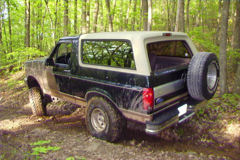 1995 Ford Bronco - A Ford Bronco navigates a muddy, wooded trail, showing off its off-road capabilities.