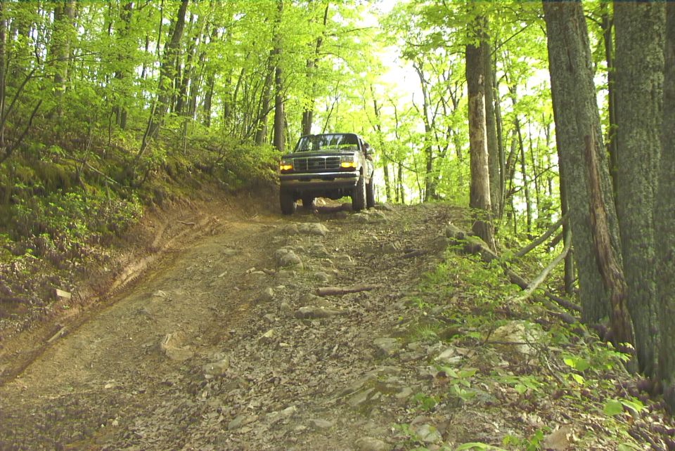 Dark green Ford Bronco driving up a rocky, wooded trail
