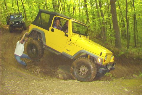 1995 Ford Bronco - A yellow Jeep Wrangler navigates a muddy trail while a person pushes from behind, with another Jeep following.
