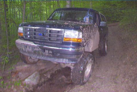 1995 Ford Bronco - 1995 Ford Bronco navigating a muddy trail through a wooded area.