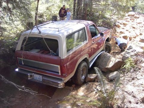 1980 Ford Bronco - A red Ford Bronco is shown navigating a difficult, rocky off-road trail with assistance from onlookers.