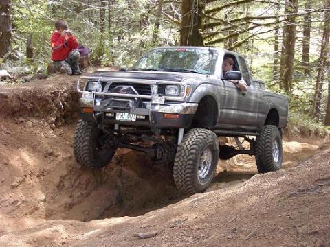 1980 Ford Bronco - Pickup truck navigates a steep dirt path in a wooded area, with a child observing the action.