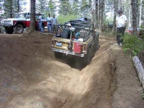 1980 Ford Bronco - Two Broncos navigate a wooded trail, one descending a steep, rutted path.