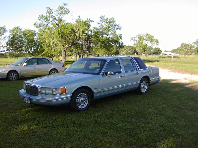 Light blue Lincoln Town Car sedan parked on grass, front-left three-quarter view