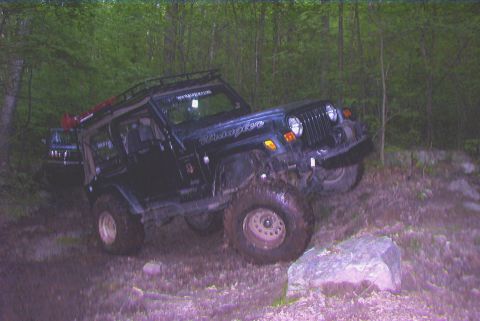 1995 Ford Bronco - A black Jeep Wrangler navigates a rocky, wooded trail with another vehicle in the background.