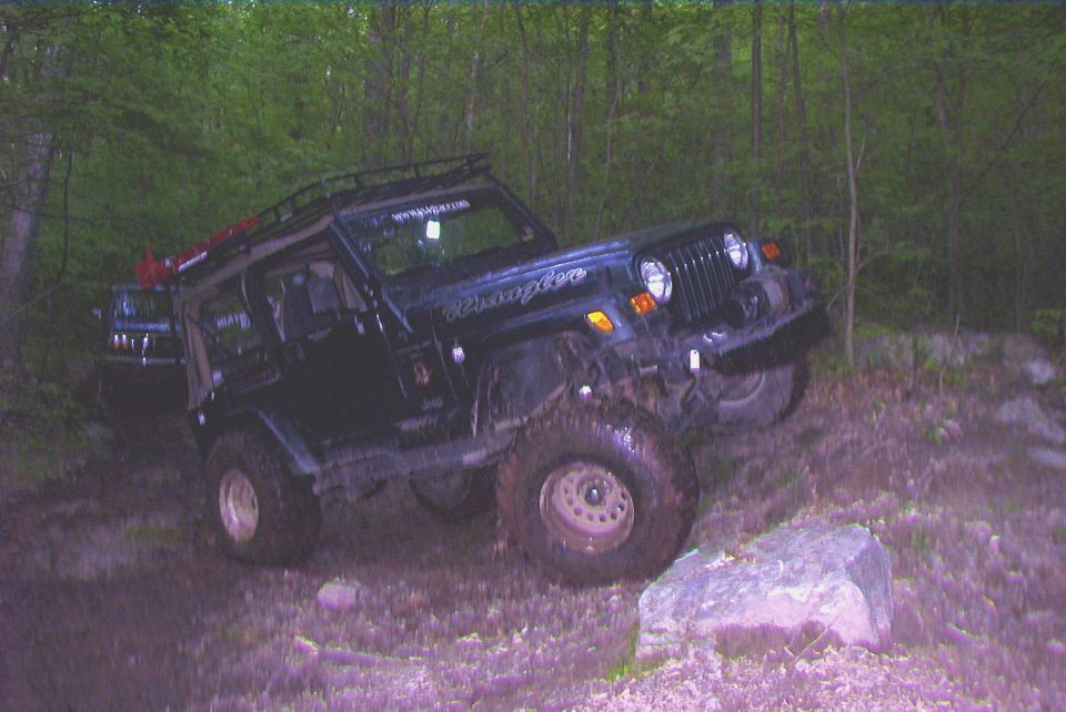Black Jeep Wrangler off-roading over rocks, another vehicle visible behind
