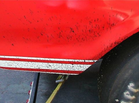 1979 Ford Bronco - Mud splatters cover the side of a red vehicle with white racing stripes, which is being supported by a jack.