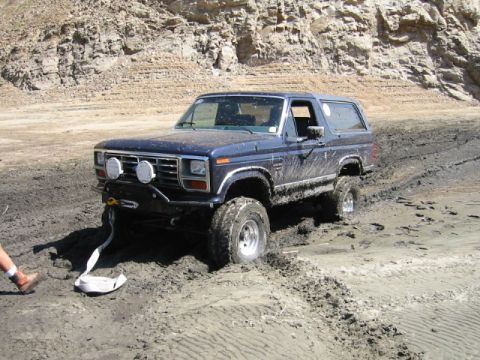 1985 Ford Bronco - Ford Bronco is stuck in the mud, with a tow strap ready to pull it out.