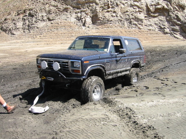 Dark blue Ford Bronco stuck in mud with recovery strap on off-road trail