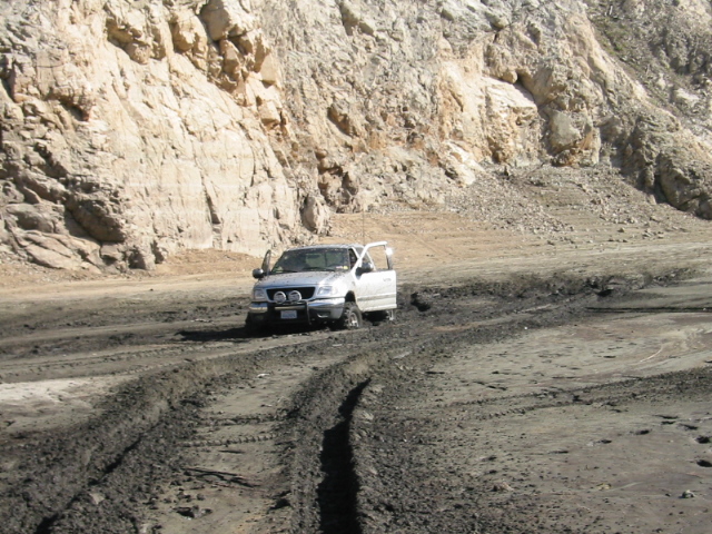 White Ford F-150 parked on muddy ground at the base of a tan rock quarry wall