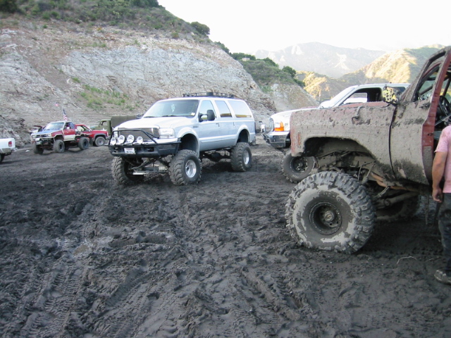 White lifted Ford Excursion and muddy 4x4 trucks parked in an off-road mud pit