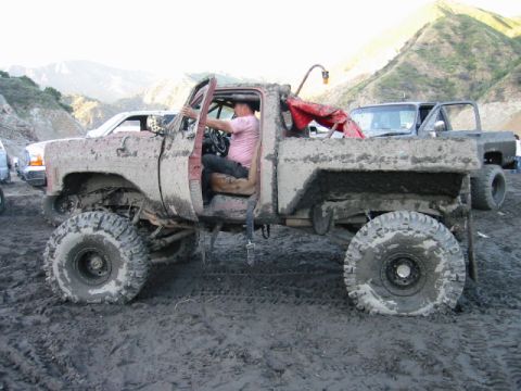 1985 Ford Bronco - A heavily mud-caked pickup truck is parked in a muddy area with a person in the driver's seat.