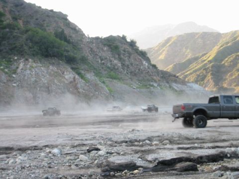 1985 Ford Bronco - Trucks navigate a dusty, rocky terrain with mountains in the background.