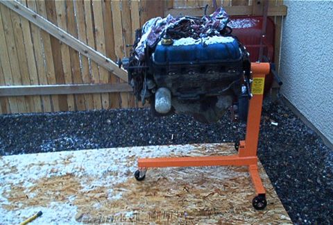 1986 Ford Bronco - Engine assembly is on an orange stand, partially covered by snow and blankets, outdoors.