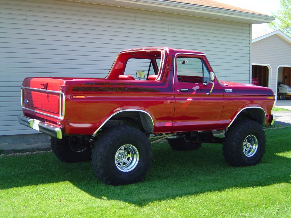 Red lifted classic Ford Bronco pickup on chrome wheels parked on grass