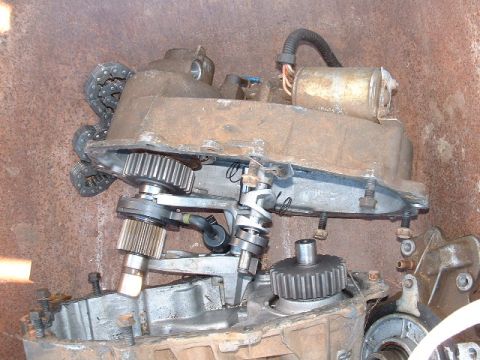 1991 Ford Bronco - A disassembled transfer case, showing internal gears and a chain, against a rusty background.