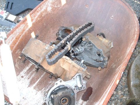 1991 Ford Bronco - Several disassembled transfer case parts, including a chain, are piled in a rusty wheelbarrow.