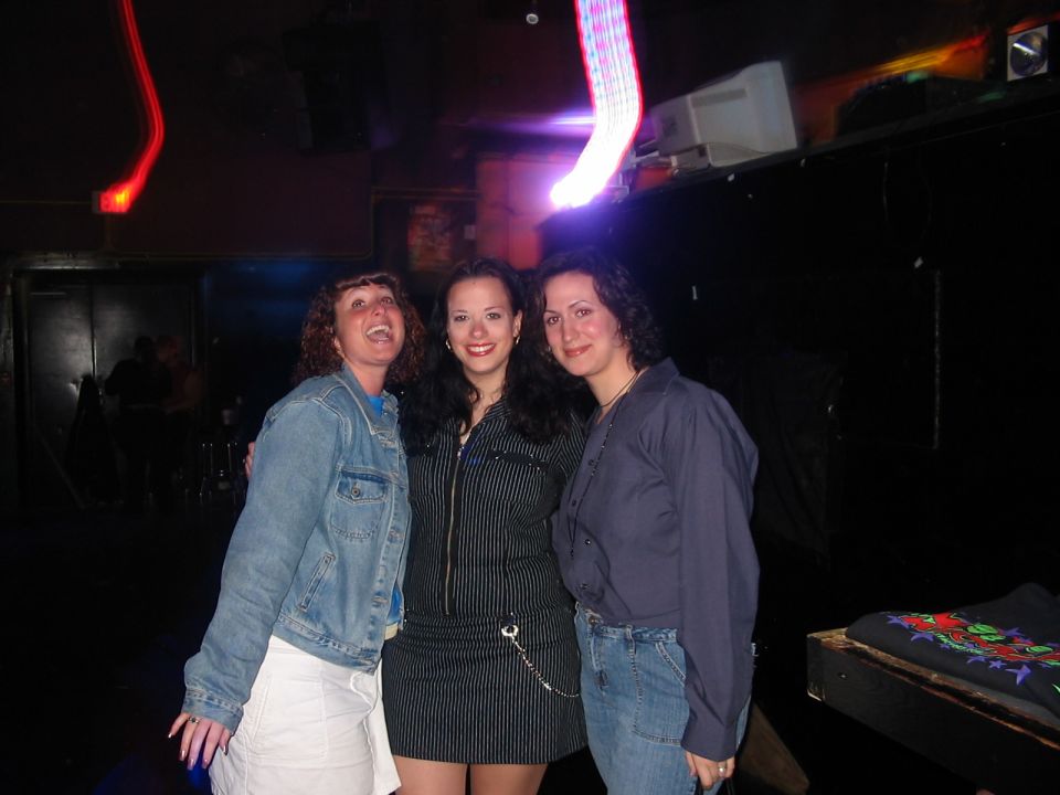 Three women posing in a nightclub with neon lights
