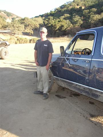 1989 Ford Bronco - A man stands beside a dark blue SUV, with another vehicle in the background on a dirt road.