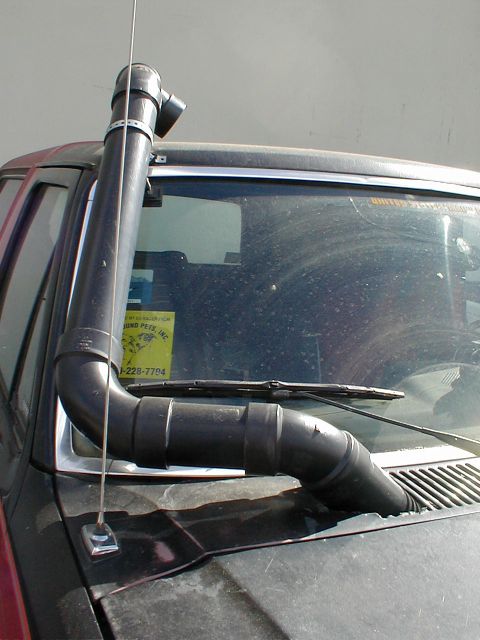 1983 Ford Bronco - Close-up of the driver's side A-pillar and windshield of a dark red/maroon SUV, showing a custom black snorkel intake tube running up the p…