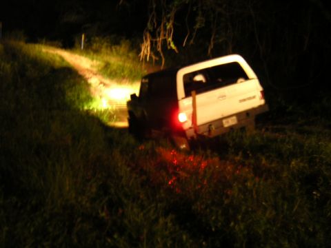 1984 Chevrolet Blazer - Pickup truck with camper shell is stuck off-road at night, its headlights illuminating the path.