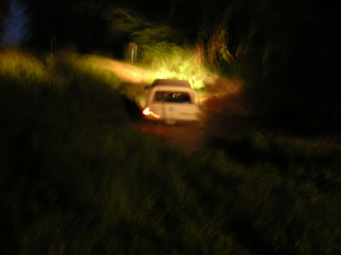 1984 Chevrolet Blazer - A white SUV navigates a dark, unpaved road at night, illuminated by its headlights.