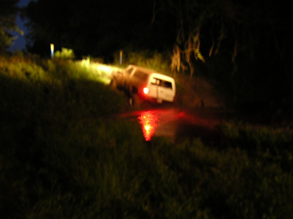 White two-door SUV backing into a water-filled mud hole at night, tail light reflecting