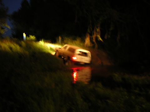 1984 Chevrolet Blazer - A white SUV navigates through a water-filled path at night, its taillights casting a red glow.