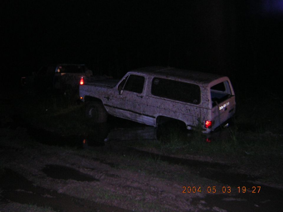Mud-covered white square-body Chevrolet K5 Blazer at night with a second truck behind