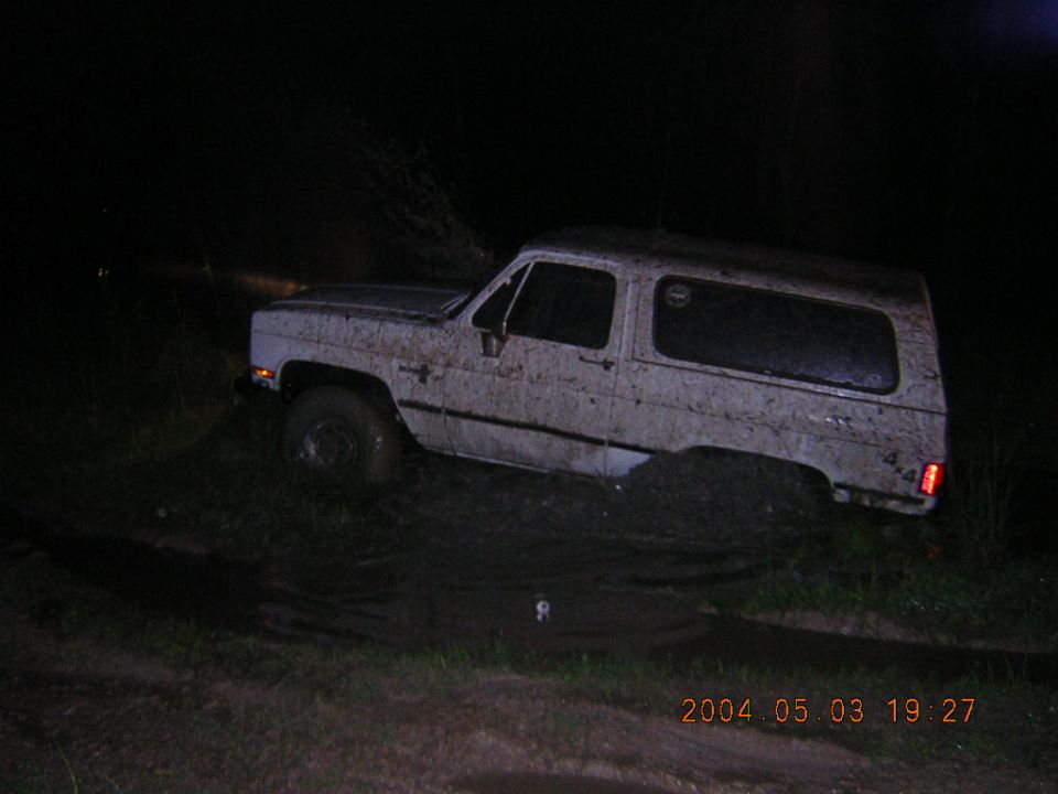 White square-body Chevrolet K5 Blazer covered in mud beside a mud hole at night