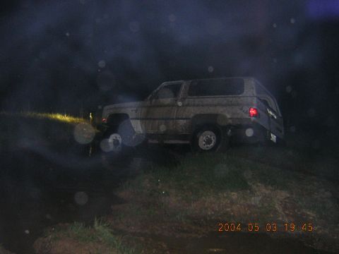1984 Chevrolet Blazer - A dirty SUV is parked on a hill at night, its headlights illuminating the dark surroundings.