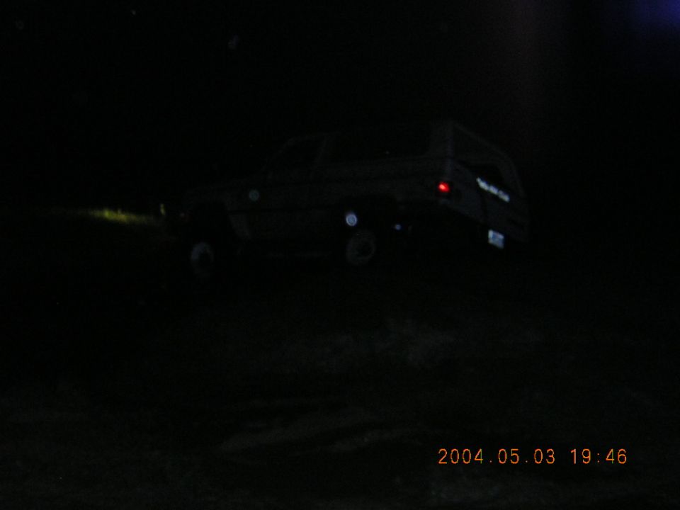 Dark night photo of a light-colored two-door SUV on a trail with tail light lit