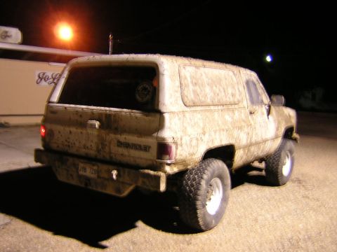 1984 Chevrolet Blazer - A heavily muddied 1984 Chevrolet K5 Blazer is seen from the rear at night, its body covered in dirt from off-road use.