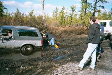 1979 Ford Bronco II - People attempt to push a Ford Bronco out of a muddy ditch while another vehicle waits.