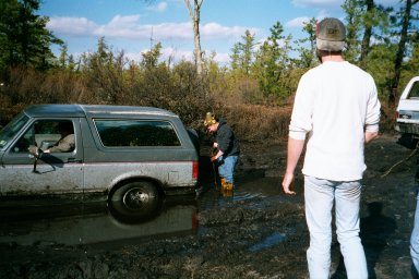 1979 Ford Bronco II - A gray Ford Bronco II is stuck in a muddy area with two people nearby and another vehicle in the background.