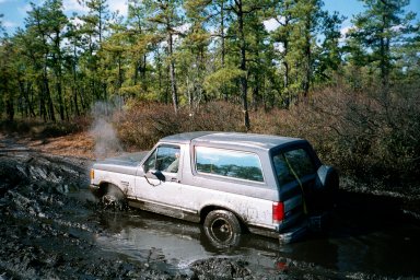 1979 Ford Bronco II - A Ford Bronco II navigates a muddy trail surrounded by trees.
