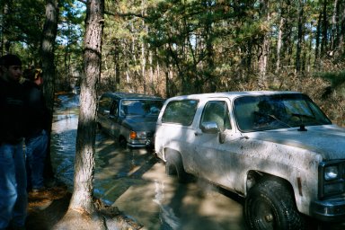 1979 Ford Bronco II - Two SUVs navigate a muddy trail through a wooded area.