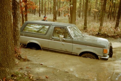 1979 Ford Bronco II - Ford Bronco is stuck in mud and trees, with a person visible in the driver's seat.