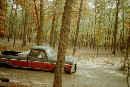 1979 Ford Bronco II - A two-tone Ford pickup truck sits off the road in a wooded area during fall.